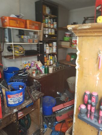 Unordentliche Werkstatt mit Regalen, Werkzeug, Schraubenziehern und Farbeimern im Raum.