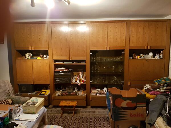 Großer Wohnzimmerschrank aus Holz mit Deko, Gläsern und Umzugskartons im Wohnzimmer.